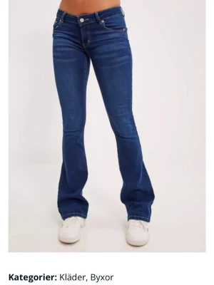 Blå bootcut jeans med låg midja - Snygga blå jeans med bootcut-snitt och låg midja. Klassisk silverfärgade knappar och kontrastsömmar. Jeansen har en smal passform upptill och blir vidare nedtill, vilket ger en cool siluett. Perfekt för dig som gillar denna stockholmstill look!