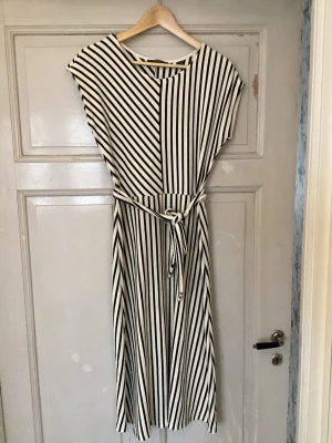 Randig långklänning med knytband från esprit  - Säljer en svartvit långklänning med snygga vertikala och diagonala ränder. Klänningen har ett smalt knytband i midjan och korta ärmar. Perfekt för dig som gillar en stilren och modern look.
