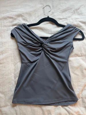 Grå omlott topp från Amisu - Snygg grå topp från Amisu i storlek S med omlott-detalj och twistad front. Toppen är ärmlös och har en mjuk, stretchig polyesterkvalitet som sitter skönt mot kroppen. Perfekt att styla med jeans eller kjol för en cool look.