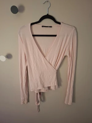 Ljusrosa omlottopp från 157 XS - Säljer en ljusrosa omlottopp från 157 i storlek XS. Toppen har lång ärm, v-ringad hals och knytband i midjan.💕 