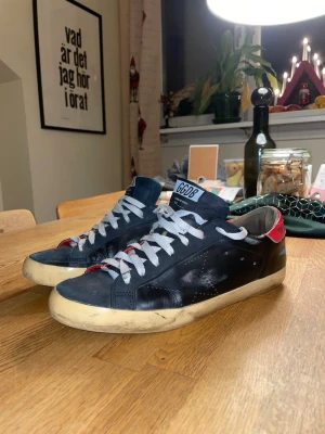 Golden Goose Superstar sneakers svart/röd - Äkta Golden Goose Superstar sneakers i svart skinn med röda detaljer på hälen och vita snören. Storlek 41 