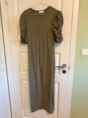 Grön långklänning med puffärm - Säljer en grön långklänning från Leveté Room (från Åhlens)  med puffiga kortärmar och ett strukturerat tyg. Klänningen har rund halsringning. Perfekt för dig som gillar unika detaljer och bekväma plagg. Använt endast en gång. Org pris: 1000 sek