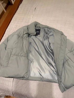 Ljusgrön pufferjacka från Monki - Säljer en ljusgrön pufferjacka från Monki med hög krage och dragkedja framtill..