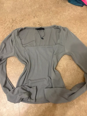 Grå långärmad topp från Amisu XS - Säljer en enkel och stilren grå långärmad topp från Amisu i storlek XS. Toppen har en tight passform och är gjord i ett mjukt, ribbat material som känns skönt mot huden. Perfekt att matcha med jeans eller kjol för en clean look.