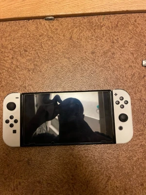 Nintendo Switch OLED - SKRIV OM DET BEHÖVS, ALLT NI SER PÅ BILDEN ÄR INKLUDERAD I KÖPET. Nintendo Switch OLED i vitt med tillhörande docka, Joy-Con straps, kontrollhållare och HDMI-kabel. Konsolen och tillbehören ser ut att vara i gott skick utan synliga skador eller större slitage. Perfekt för både handhållet och stationärt spelande.