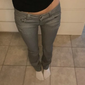 Gråa bootcut jeans med låg midja - Snygga grå jeans med låg midja och bootcut-ben. Klassisk femficksmodell med dragkedja och knapp framtill. Jeansen har en rak passform upptill och lätt utsvängda ben, vilket ger en cool siluett. Perfekta för dig som gillar en avslappnad men trendig look.