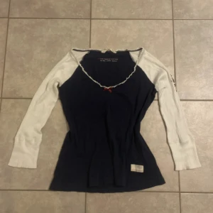 Mörkblå och vit långärmad topp med rosett - Supersöt långärmad topp från ODD MOLLY i mörkblått med vita ärmar. Ribbad struktur, dekorativ röd rosett vid halsen och broderad kompass med texten 'LOVE' på ena ärmen. Söt spetskant runt.