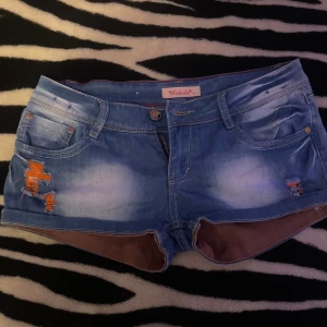 Blå jeansshorts från Michelle - Säljer ett par blå jeansshorts från Michelle med slitna detaljer och orange tråd på framsidan. Shortsen har klassisk femficksdesign, låg midja och bruna inslag på insidan av benen. Perfekta för en avslappnad sommarstil.FRÅN ITALIEN 🇮🇹 PRIS KAN DISKUTERAS💗💗