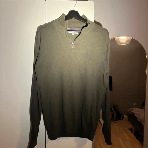 Grön half zip tröja från U.S. Polo Assn. - Snygg mörkgrön långärmad tröja från U.S. Polo Assn. med half zip och liten broderad logga på bröstet. Tröjan har ribbad krage och är tillverkad i mjuk bomull, perfekt för dig som gillar klassisk stil med sportig touch.