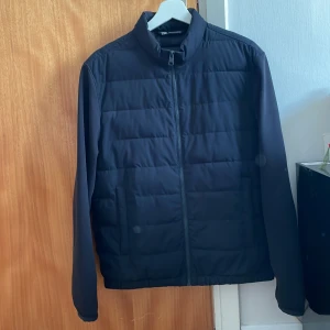 Svart pufferjacka från Zara, M - Svart pufferjacka från Zara i storlek M. Jackan har quiltad design, ståkrage och hel dragkedja framtill. Tillverkad i syntetmaterial, perfekt för kyliga dagar. Stilren och enkel look med långärmade ärmar och två sidofickor.
