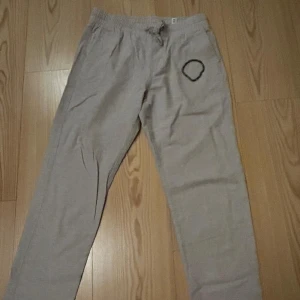 Beige linnebyxor från Jack & Jones - Snygga beige linnebyxor från Jack & Jones med elastisk midja och snörning. Byxorna har en avslappnad passform. Perfekta för chill dagar och sommarhäng.