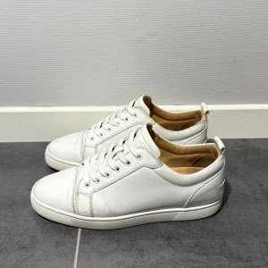Christian Louboutin  - Fräscha vita sneakers i skinn med klassisk rund tå och platt sula. Skorna har vit snörning och diskreta sömmar som ger en stilren look. Insidan är ljusbeige och de har en enkel design som passar till många olika outfits.