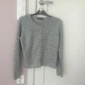 Grå kofta från 157 med knappar - Mysig grå kofta från 157 i storlek S. Koftan har rund halsringning, långa ärmar och knäppning med fem knappar framtill. Materialet är stickat och känns mjukt mot huden, perfekt för lager-på-lager under kyliga dagar.