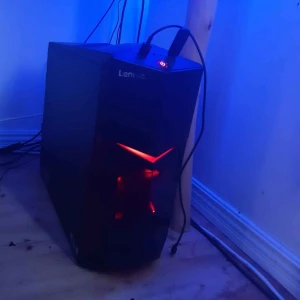 Lenovo stationär gamingdator - Lenovo stationär dator med modern design och röd LED-belysning. Perfekt för gaming eller arbete. Chassit ser ut att vara i gott skick utan synliga repor eller skador. Flera portar på ovansidan för enkel anslutning av tillbehör.