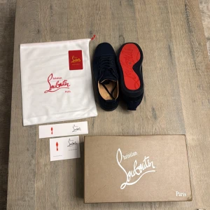Mörkblå mocka sneakers Christian Louboutin - Snygga mörkblå sneakers från Christian Louboutin i mjuk mocka med klassisk röd sula och broderad logga på hälen. Skorna har rund tå, snörning och platt sula. Kommer med originalkartong, dustbag och äkthetskort. Perfekt för dig som gillar exklusiv streetstyle.