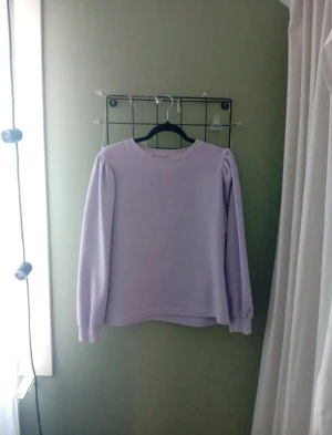 Ljuslila långärmad tröja - Säljer en ljuslila långärmad tröja med puffade axlar och rund hals. Tröjan har en enkel och clean design som ger en soft vibe. Perfekt för dig som gillar pastellfärger och vill ha något bekvämt och snyggt i garderoben.