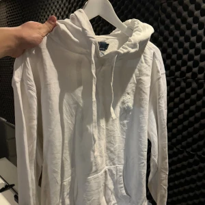 Vit hoodie från Polo Ralph Lauren - Vit hoodie från Polo Ralph Lauren med huva och snörning. Tröjan har en klassisk känguruficka framtill och är tillverkad i en mjuk blandning av bomull, polyester och viskos. Perfekt för chill dagar och enkel att matcha med jeans eller joggers.