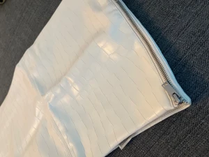 Vit kort kjol från H&M DIVIDED - Säljer en vit kort kjol från H&M DIVIDED i storlek 38. Kjolen har en glansig yta med croco-präglat mönster och en snygg dragkedja i sidan. Materialet är syntet och polyester, vilket ger en cool och modern look. Perfekt för dig som gillar trendiga detaljer.