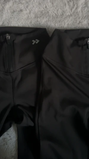 Svarta bootcut träningsbyxor från Lager 156 - Säljer tre par svarta bootcut träningsbyxor från Laget 156. Byxorna har hög midja, dragkedjor framtill och är gjorda i ett stretchigt syntetmaterial som passar perfekt för sportiga aktiviteter. Snyggt logotryck på höften och stilren design.