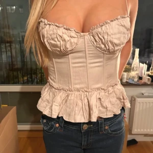 Beigerosa korsett med volang  - Söt beige korsett med tunna axelband och volangkant nedtill.  Storlek 36, i använt skick, finns ett litet hål vid kupan men i övrigt fin och hel 💗