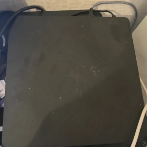 PlayStation 4 med handkontroll och spel - PlayStation 4 säljes med en vit DualShock 4-kontroll (vänster handtag tejpat) och två populära spel: Mortal Kombat och Red Dead Redemption II. Konsolen har synliga fingeravtryck och lätt slitage, men är fullt fungerande. Perfekt för dig som vill börja spela direkt!