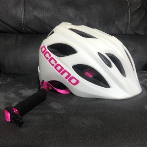 Vit cykelhjälm från Occano S/M - Snygg vit cykelhjälm från Occano med rosa detaljer och justerbart spänne. Ventilerad design för extra komfort och MIPS-teknologi för ökad säkerhet. Passar juniorer och har en lätt vikt på ca 250g. Perfekt för dig som vill ha både stil och skydd på cykelturen.