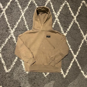 Beige hoodie från Warp med huva - Säljer en beige hoodie från Warp med stilren WA-logga på bröstet. Tröjan har en stor huva, ribbade muddar och är tillverkad i mjuk bomull och polyester. Perfekt för chill dagar och har en relaxed passform som är skön att bära.
