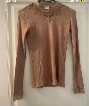Beige ribbad topp med spets från VRS Teen - Supersnygg rosa ribbad topp från VRS Teen med långärmad passform. Spetsdetaljer vid halsringning och ärmslut ger en extra touch. Perfekt för dig som gillar romantisk stil och vill ha något som sticker ut lite extra.