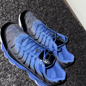 Blå och svarta sneakers med snörning - Säljer ett par snygga sneakers i blått och svart med coolt mönstrad ovandel och snörning. Skorna har en rund tå, platt sula och detaljer i blankt syntetmaterial. Insidan är mjukt vadderad för extra komfort och yttersulan har ett sportigt mönster.