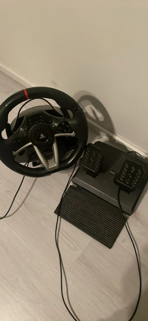PlayStation Racing Wheel och Pedaler - Snyggt PlayStation ratt och pedalset för racing-spel. Komplett med kablar, knappar och PlayStation-logga. Passar perfekt för realistisk spelupplevelse. Produkten ser ut att vara i gott skick utan synligt slitage eller defekter. Annat pris kan diskuteras
