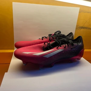 Adidas X Speedflow rosa fotbollsskor - Säljer ett par Adidas X Speedflow fotbollsskor i en snygg rosa och svart färg med vita detaljer. Skorna har snörning, metall-dobbar och en strömlinjeformad design för maxad fart på planen. Ovandelen är tillverkad i syntetmaterial och har en låg profil.