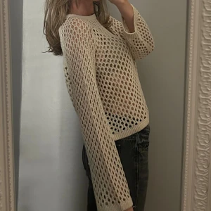 Beige stickad meshtröja med hålmönster - Säljer en beige stickad tröja med coolt hålmönster i meshstil. Tröjan har långärmade och lite loose passform, perfekt att styla över ett linne eller bralette. Ribbad kant vid hals, ärmslut och nederkant. Superfräsch och trendig vibe.