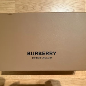 Burberry ”Stevie” sneaker  - Snygga Burberry sneakers med klassiskt rutigt mönster i beige, svart och rött på sidorna. Ovandel i svart skinn och mocka, vita platta sulor och svarta snören. Perfekt för dig som gillar lyxiga detaljer och stilren design. 
