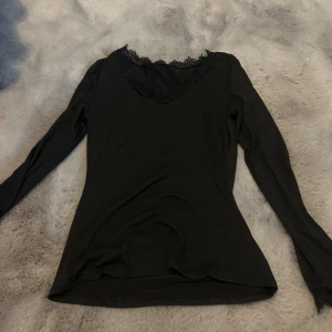 Svart långärmad topp med spets - Svart långärmad topp med v-ringning och snygg spetsdetalj runt halsen. Toppens material känns mjukt och följsamt, perfekt för en stilren look. Passformen är normal och toppen är enkel att matcha med olika outfits. En doup på intimissimis tröja, lite tjockare material. Endast testad
