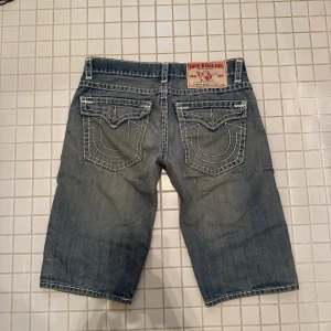 True Religion jeansshorts blå strl 36 - Säljer ett par blå jeansshorts från True Religion i storlek 36. Klassisk femficksmodell med kontrastsömmar och ikoniska bakfickor med broderad design. 
