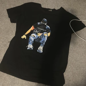 Svart t-shirt med tryck Sneaker Myth - Svart t-shirt från Sneaker Myth med coolt tryck av en person i streetwear på framsidan. Klassisk rund hals och korta ärmar. Materialet är mjukt och känns som bomull, perfekt för en avslappnad stil.