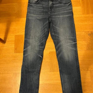 Tommy Hilfiger blå jeans, stl 164 - Snygga blå jeans från Tommy Hilfiger i storlek 164. Klassisk femficksmodell med raka ben och diskreta slitningar framtill. Jeansen har normal passform och är tillverkade i mjukt denimtyg med stretch för extra komfort.