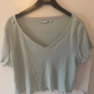 Ljusgrön ribbad croppad topp 157 - Säljer en ljusgrön croppad topp från 157 med v-ringning och korta ärmar. Toppen är ribbad och har vågiga kanter vid ärmslut och nederkant för en extra söt touch. Perfekt för dig som gillar en enkel men trendig stil.