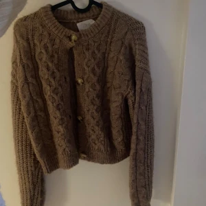Beige stickad kofta från Zara - Kofta från Zara som passar storlek xs! Mysig beige stickad kofta från Zara med grovt flätmönster och snygga guldfärgade knappar framtill. Rund halsringning och långa ärmar.