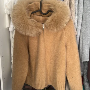 Beige pälsjacka med fluffig krage - Säljer en beige pälsjacka med superfluffig krage och dragkedja framtill. Jackan har långärmade ärmar och ribbad nederkant, perfekt för dig som vill ha en mysig och snygg look under kyliga dagar.