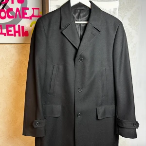 Svart rock från Dressmann i ullblandning - Svart rock från Dressmann med klassisk krage och tre knappar framtill. Jackan har två fickor med lock och innerficka med knapp. Tillverkad i ullblandning med slät finish och fodrad insida. Medföljer extra knappar. Perfekt för dig som gillar stilrena och tidlösa plagg.