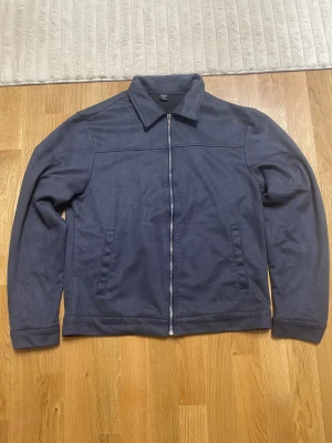 Mörkblå overshirt från H&M - Snygg mörkblå overshirt från H&M med klassisk krage och raka linjer. Jackan har dragkedja framtill och två sidofickor. Materialet är mjukt och känns som syntet, perfekt för lager-på-lager. Enkel och stilren design som funkar till många outfits.