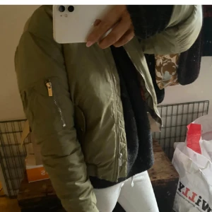 Grön bomberjacka med orange foder - Säljer en grön bomberjacka med coolt orange quiltat foder. Jackan har dragkedja framtill och på ärmen, samt ribbade muddar vid handleder och midja. Perfekt för dig som gillar streetstyle och vill sticka ut med färg på insidan.
