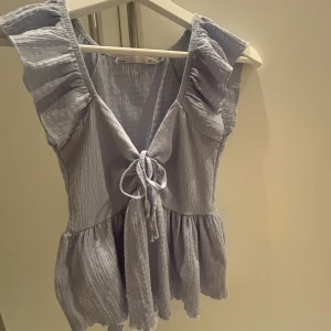 Ljusblå volangblus  - Söt ljusblå topp som har volangdetaljer vid axlarna, knyt framtill och är tillverkad i ett mjukt, krinklat tyg. Modellen är ärmlös. I storlek XS men passar mig perfekt med storlek S!🩵💙Skriv för mer.