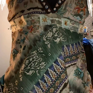 Vintage topp från Miss Swan - Unik vintage topp från Miss Wan med tunna axelband, v-ringning dekorerad med pärlor och glittriga detaljer. Klänningen har ett färgstarkt blommigt och paisleymönster i grönt, beige, blått och orange samt dekorativa band med broderade stjärnor. Lätt och luftig i materialet, perfekt för dig som vill stå ut! Pris går att diskuteras. Storleken är S men tror också den skulle passa M men är ej 100% säker.