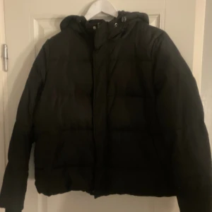 Svart pufferjacka med huva - Svart pufferjacka med huva och quiltad design. Jackan har en loose passform. Den har långa ärmar och dragkedja framtill, samt snörning vid huvan för extra komfort. Jackan är från VeroModa i storlek M och använd fåtal gånger förra året. Pris går att diskutera vid snabb affär och har möjlighet att skicka samma dag☺️