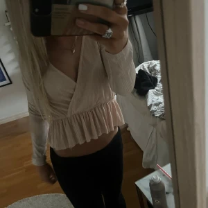 Blus gina - Säljer en champagnefärgad omlottopp från Gina Tricot i storlek XS. Toppen har långärmade ärmar, v-ringning och volang nedtill. Materialet är glansigt med smala vertikala ränder som ger en lyxig känsla. Perfekt för dig som gillar feminina detaljer och snygg passform.