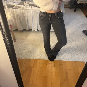 Mörkgrå jeans från Gina Tricot - Snygga mörkgrå jeans från Gina Tricot med raka ben och klassisk femficksmodell. Jeansen har dubbla silverfärgade knappar i midjan och tydliga sömmar. Perfekta för dig som gillar en enkel men stilren look.