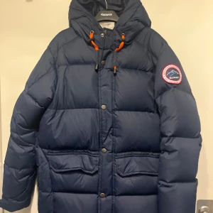 Mörkblå dunjacka från Tuxer - Mörkblå dunjacka från Tuxer med huva och orange snörningsdetaljer. Använd fåtals gånger, mycket fint skick 