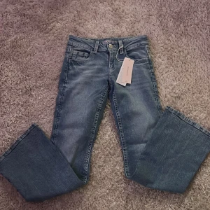 Blå flare jeans med broderade fickor - Snygga ljusblå flare jeans med låg midja och broderade bakfickor med paljettdetaljer. Jeansen har klassisk femficksdesign, knapp- och dragkedjestängning samt dekorativa sömmar. 